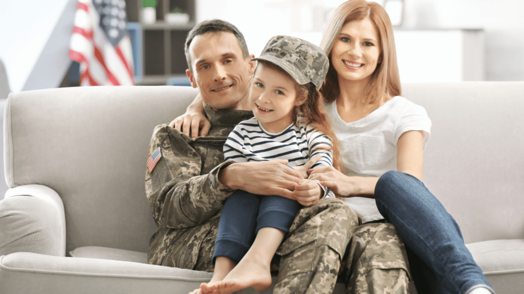 a family of three sit on a couch together, the father is dressed in a military uniform