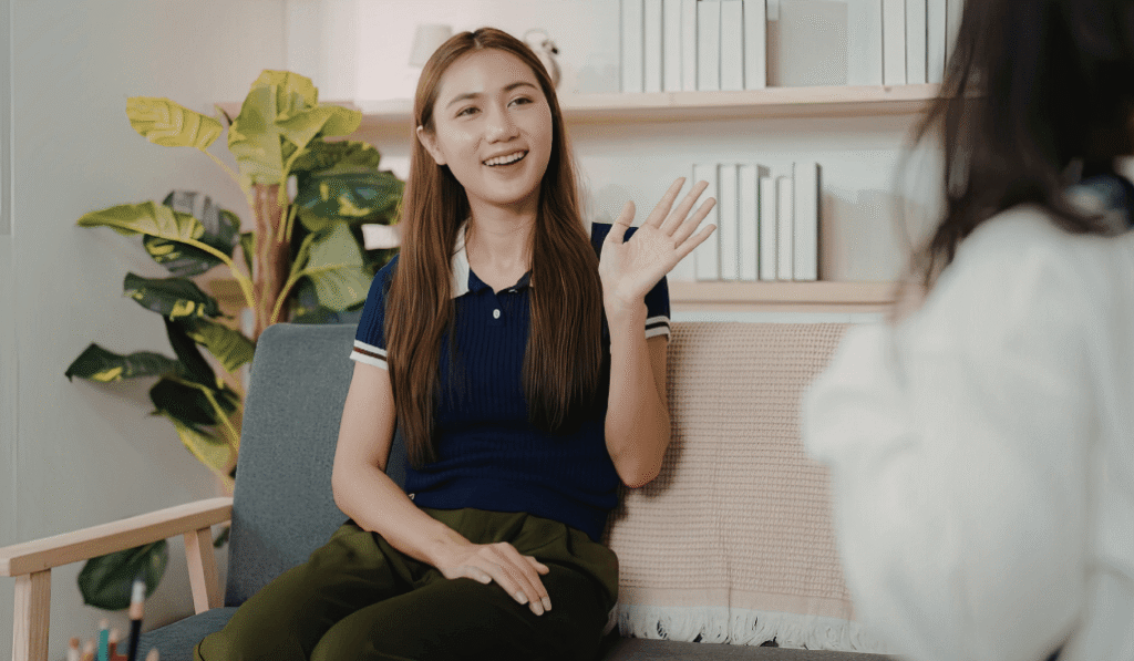 Women sitting on a couch smiling and waving hello to someone sitting across from her