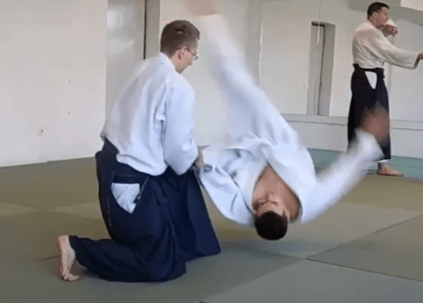 Two people practicing aikido on a mat, with one person being thrown over the other's shoulder.